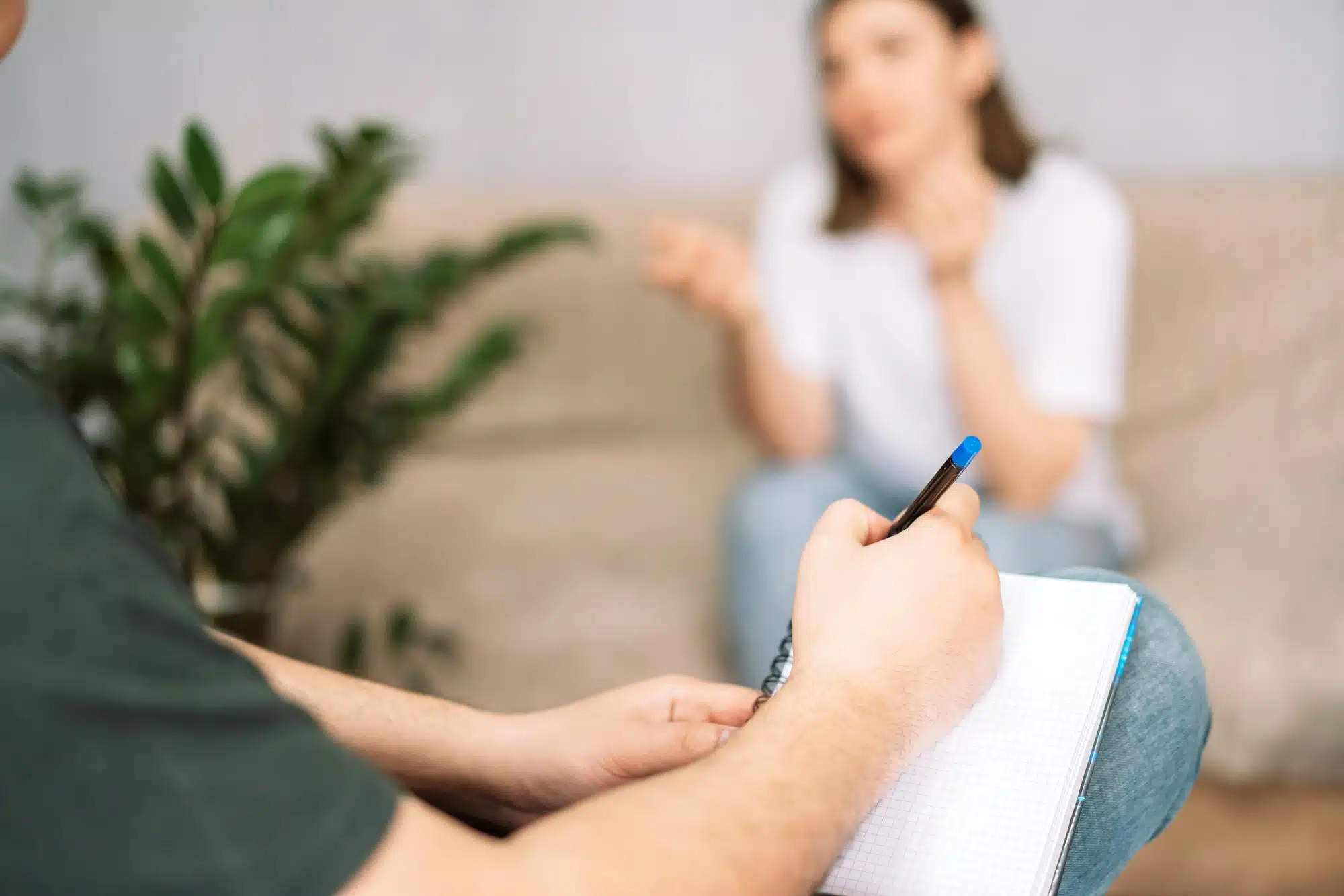 Psicólogo anotando en una libreta los problemas que le cuenta su paciente en una sesión de terapia individual